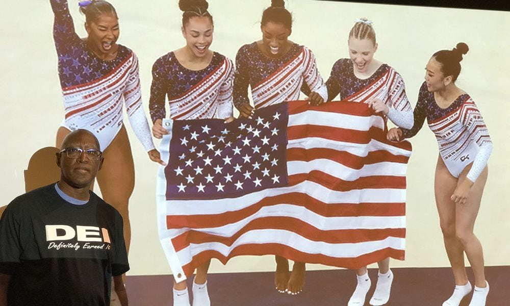 Michael Carter, the Chief Diversity Officer at Sinclair Community College and once the head basketball coach at Springfield South and Trotwood Madison high schools, stands in front of a photo of the gold-medal winning U.S. womens gymnastics team at the 2024 Olympic Games in Paris. The quintet (left to right) Jodan Sparks, Hezly Rivera, Simone Biles, Jade Carey and Suni Lee are the most racially-diverse team in U.S. Olympic history and were one of the examples Carter used in his presentation last week about the way sports has been at the forefront of the positive results that come from DEI (Diversity, Equity and Inclusion) Tom Archdeacon/CONTRIBUTED