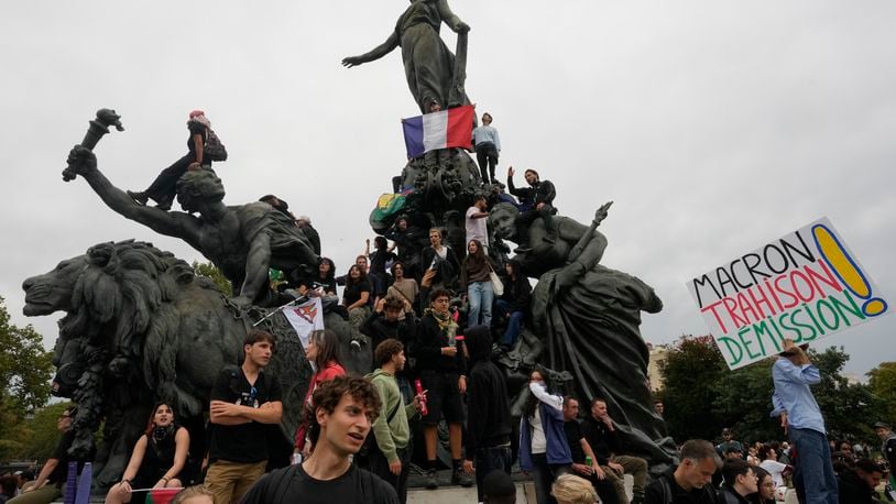 Demonstrators, one displaying French flag, gather under the statue of Marianne, a symbol of the French Republic, during a protest demonstration responding to a call from the far-left party leader who criticized as a power grab the president's appointment of a new prime minister, Michel Barnier, in Paris, France, Saturday, Sept. 7, 2024. (AP Photo/Michel Euler)