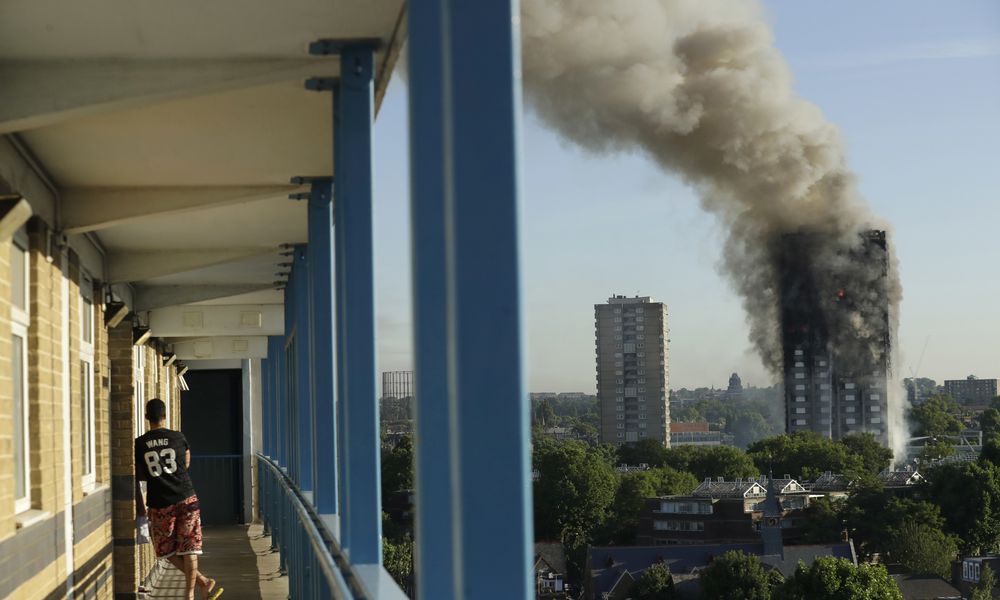 FILE - A resident in a nearby building watches smoke rise from the Grenfell Tower building on fire in London, Wednesday, June 14, 2017. (AP Photo/Matt Dunham, File)