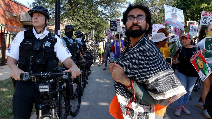 YM Masood, 20, right, stands next to a line of Chicago police officers during a March on DNC protest on Monday, Aug. 19, 2024, in Chicago, as he serves as a volunteer marshal for several of the protests to help keep protesters organized and safe and deescalate potential conflict. (AP Photo/Martha Irvine)