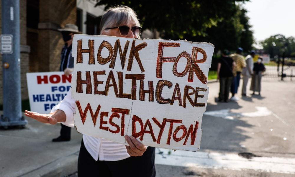 Kathleen Galt, from Dayton, along with other protesters carry signs near the site of the now demolished Good Sam Hospital Friday July 23, 2021. A press conference was held moments later where community leaders and clergy talked about Premier Health's plan to build an urgent care facility on the site. JIM NOELKER/STAFF