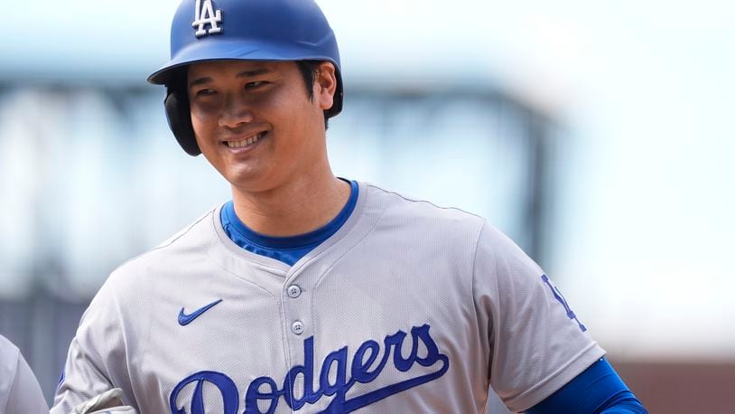 Los Angeles Dodgers' Shohei Ohtani smiles after reaching first base on a single off Colorado Rockies relief pitcher Seth Halvorsen in the eighth inning of a baseball game Sunday, Sept. 29, 2024, in Denver. (AP Photo/David Zalubowski)