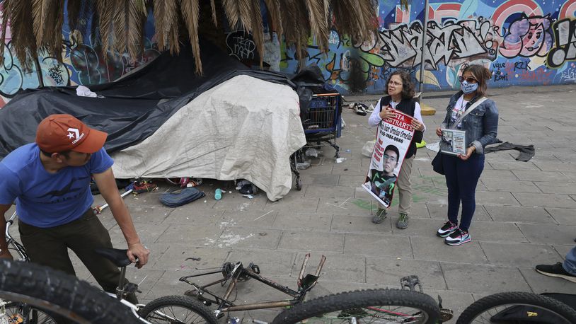 Catholic nun Paola Clericó, holding a poster of missing person Fernando Ivan Ornelas, and Veronica Rosas with a photo of her missing son Diego, ask a resident if he recognizes either man and invite him to join a Mass with members of their search collective "Uniendo Esperanzas" or Uniting Hope, in Mexico City, Sunday, July 21, 2024. The collective of people with missing family members held a Mass on the birthday of Ornelas who disappeared five years prior. (AP Photo/Ginnette Riquelme)