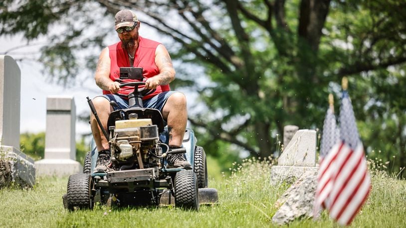 Volunteer Andy Jones cuts the grass at Bear Creek Hill Grove Cemetery on Union Road in Trotwood on Thursday, July 20, 2023. The city of Trotwood has filed a lawsuit against the cemetery citing resident complaints about maintenance and upkeep. JIM NOELKER/STAFF