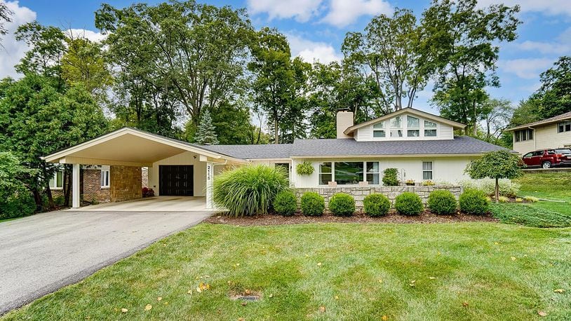 The front of the mid-century modern tri level has a stone accent wall, attached carport and one car attached garage and picture window