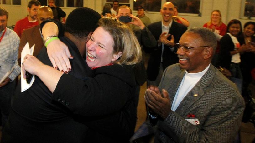 Mayor elect Nan Whaley is hugged by Dayton city commissioner Joey Williams while Jeff Mims (right) applauds Tuesday night at Democratic headquarters in Dayton. Both Williams and Mims won a seat on the city commission. LISA POWELL / STAFF