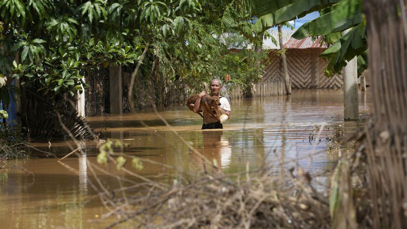 A man carrying a dog wades through a flooded road in Naypyitaw, Myanmar, Saturday, Sept. 14, 2024. (AP Photo/Aung Shine Oo)