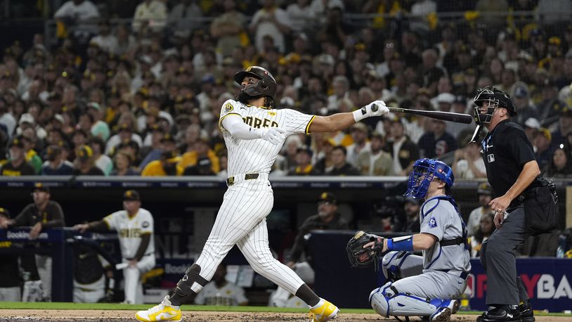 San Diego Padres' Fernando Tatis Jr., left, follows through on his two-run home run as Los Angeles Dodgers catcher Will Smith, center, and home plate umpire Cory Blaser watch during the second inning in Game 3 of a baseball NL Division Series, Tuesday, Oct. 8, 2024, in San Diego. (AP Photo/Gregory Bull)