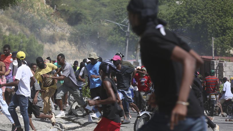 People run from tear gas fired by police to disperse protesters demanding police and the Prime Minister take immediate action against gangs in Port-au-Prince, Haiti, Monday, Aug. 19, 2024. (AP Photo/Odelyn Joseph)