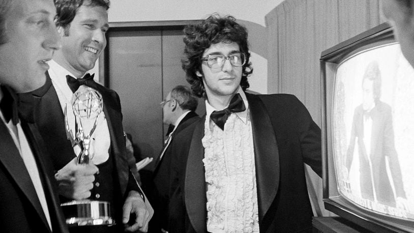 FILE - Chevy Chase, a cast member on "Saturday Night Live," holds his Emmy Award as he watches a monitor showing producer Lorne Michaels accepting another Emmy for the show, while writers Alan Zweibel, left, and Tom Davis, right, look on, during the 28th Primetime Emmy Awards in Los Angeles on May 17, 1976. (AP Photo/Reed Saxon, File)