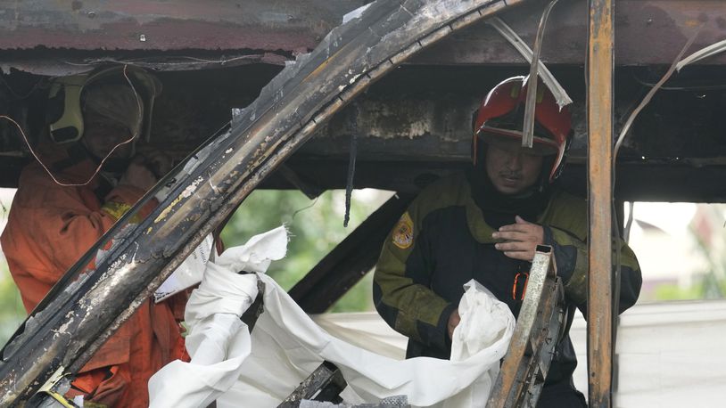 Rescuers hold a white cloth to cover the body of a victim inside a bus that caught fire, carrying young students with their teachers, in suburban Bangkok, Tuesday, Oct. 1, 2024. (AP Photo/Sakchai Lalit)