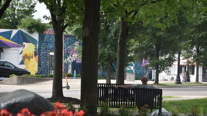 A man sits on a bench in a small park on South Patterson Boulevard in downtown Dayton. The park has multiple trees that provide good shade. CORNELIUS FROLIK / STAFF
