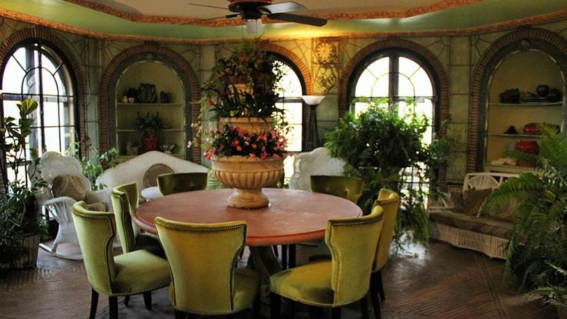 An octagonal conservatory features leaded glass French doors framed by brick-trimmed arches, iron trellises, herringbone brick flooring, molded plaster trim with floral motifs and abundant natural light to nurture various plants.