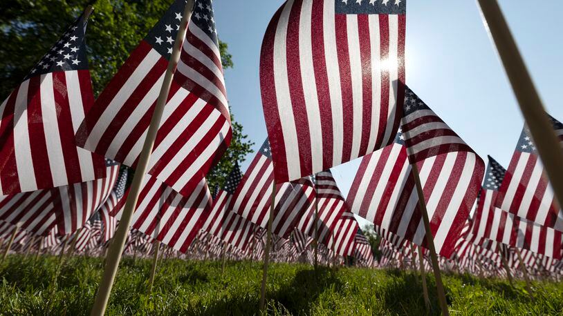 FILE - The sun shines through the flags in the Memorial Day Flag Garden on Boston Common, May 27, 2023, in Boston. Memorial Day is supposed to be about mourning the nation’s fallen service members. But it’s come to anchor the unofficial start of summer and retail discounts. (AP Photo/Michael Dwyer, file)
