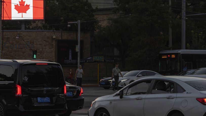 A Chinese paramlitary policeman crosses the road near vehicles outside the Canadian embassy in Beijing, Tuesday, Aug. 27, 2024. (AP Photo/Ng Han Guan)