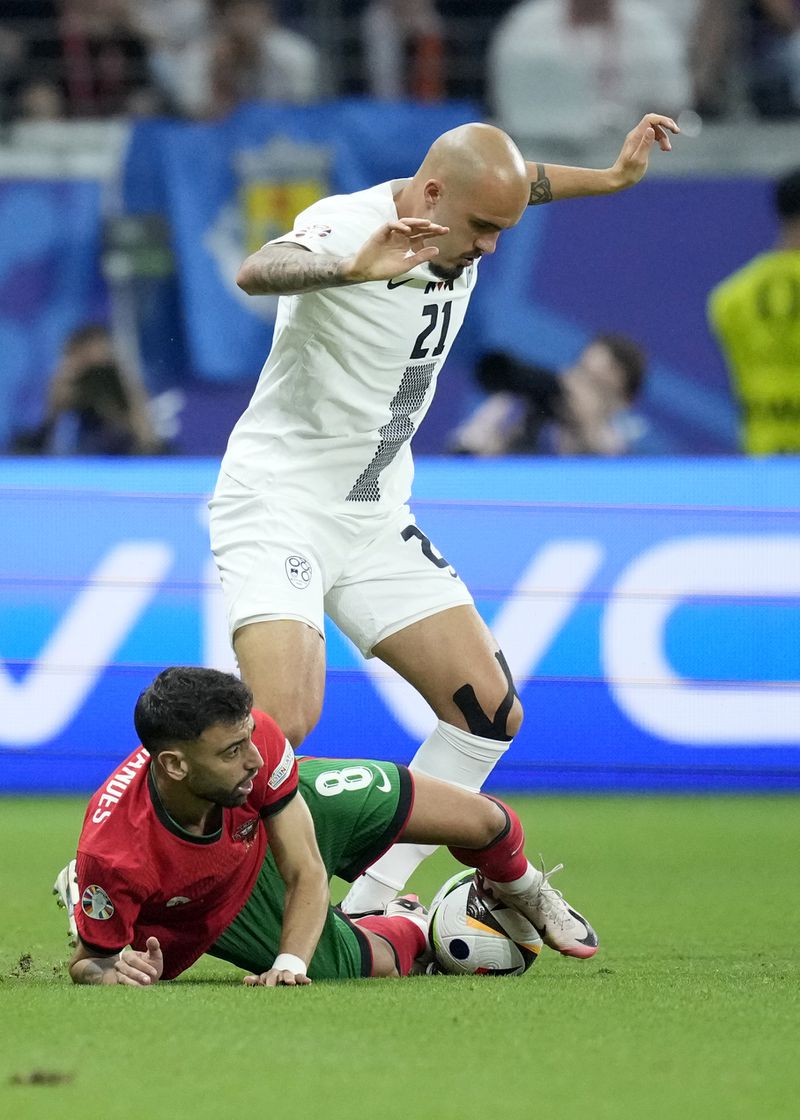 Portugal's Bruno Fernandes, bottom, challenges for the ball with Slovenia's Vanja Drkusic during a round of sixteen match between Portugal and Slovenia at the Euro 2024 soccer tournament in Frankfurt, Germany, Monday, July 1, 2024. (AP Photo/Ebrahim Noroozi)