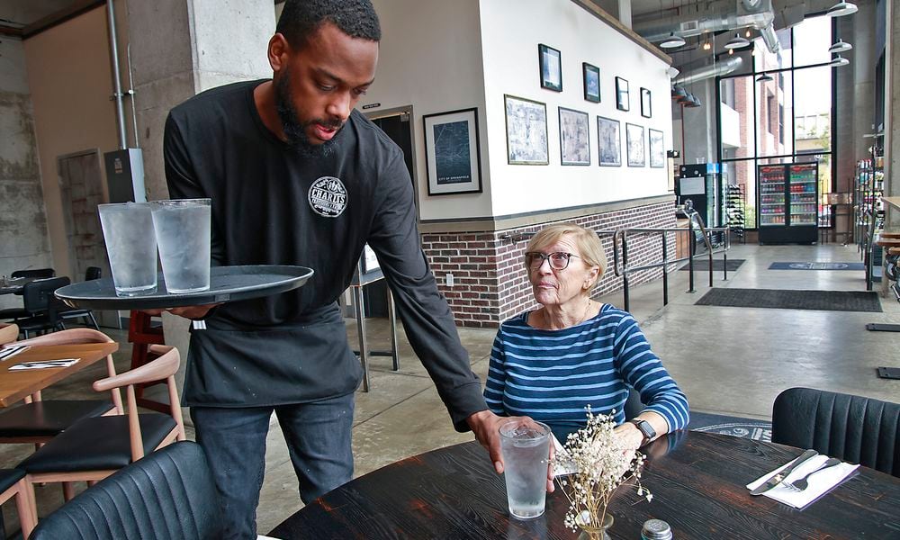 Demetrius Jones, a waiter at Charlo's Provisions & Eatery in downtown Springfield, delivers drinks to Kim VanOsdell's table Wednesday, August 7, 2024. BILL LACKEY/STAFF