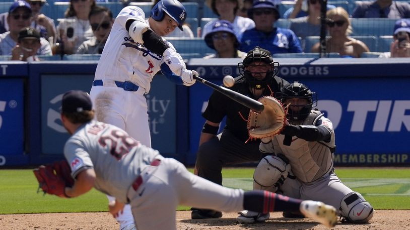 Los Angeles Dodgers' Shohei Ohtani, second from left, hits a solo home run as Cleveland Guardians starting pitcher Tanner Bibee, left, watches along with catcher Bo Naylor, right, and home plate umpire Dan Bellino during the fifth inning of a baseball game, Sunday, Sept. 8, 2024, in Los Angeles. (AP Photo/Mark J. Terrill)