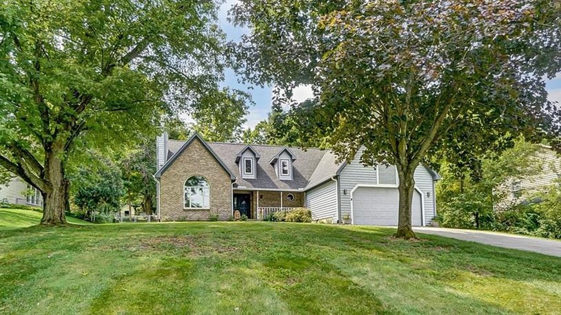 The front of the brick and wood cape cod style story and a half has two dormer windows, a two car attached garage and a covered front porch with railings.