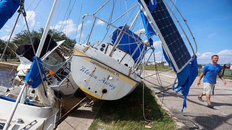 Drew Griffith walks past three boats that washed up against the seawall in the aftermath of Hurricane Helene at the Davis Islands' Seaplane Basin near Peter O. Airport Friday, Sept. 27, 2024 in Tampa, Fla. (Chris Urso/Tampa Bay Times via AP)