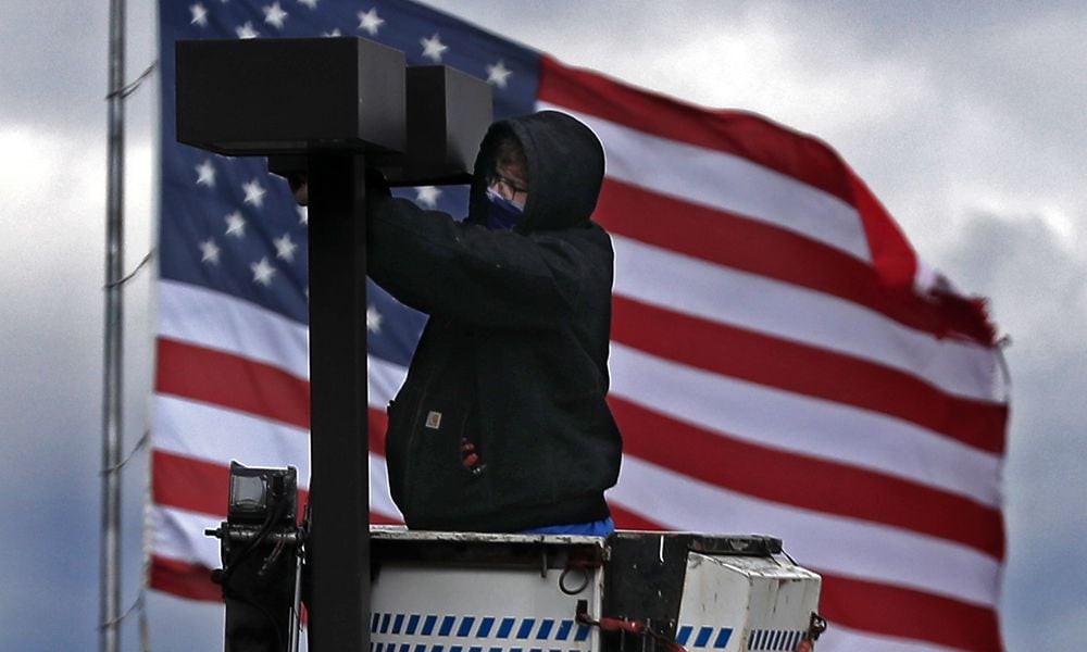 The giant American flag at the Springfield Post Office provided a patriotic backdrop for a worker fixing a light in the parking lot of Shawnee Place Apartments in downtown Springfield. BILL LACKEY/STAFF