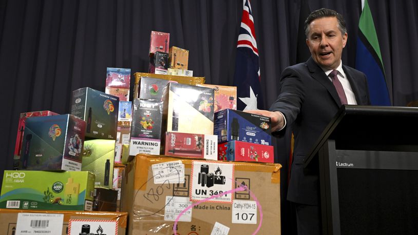 Australian Health Minister Mark Butler speaks gestures towards boxes of electronic cigarettes during a press conference at Parliament House in Canberra, Australia, Wednesday, Feb. 28, 2024. Australia announced plans, Monday, June 24, to outlaw the sale of vapes outside pharmacies from next week under some of the world's toughest restrictions on electronic cigarettes. (Lukas Coch/AAP Image via AP)