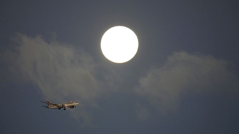 A Qatar Airways jetliner approaches for landing in Lisbon, with a supermoon in the background, at sunrise Tuesday, Aug. 20, 2024. (AP Photo/Armando Franca)