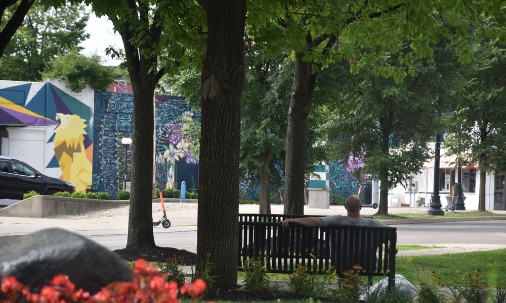 A man sits on a bench in a small park on South Patterson Boulevard in downtown Dayton. The park has multiple trees that provide good shade. CORNELIUS FROLIK / STAFF