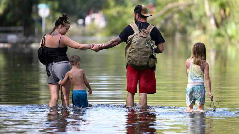 FILE - Dustin Holmes, second from right, holds hands with his girlfriend, Hailey Morgan, while returning to their flooded home with her children Aria Skye Hall, 7, right, and Kyle Ross, 4, in the aftermath of Hurricane Helene, Sept. 27, 2024, in Crystal River, Fla. (AP Photo/Phelan M. Ebenhack, File)