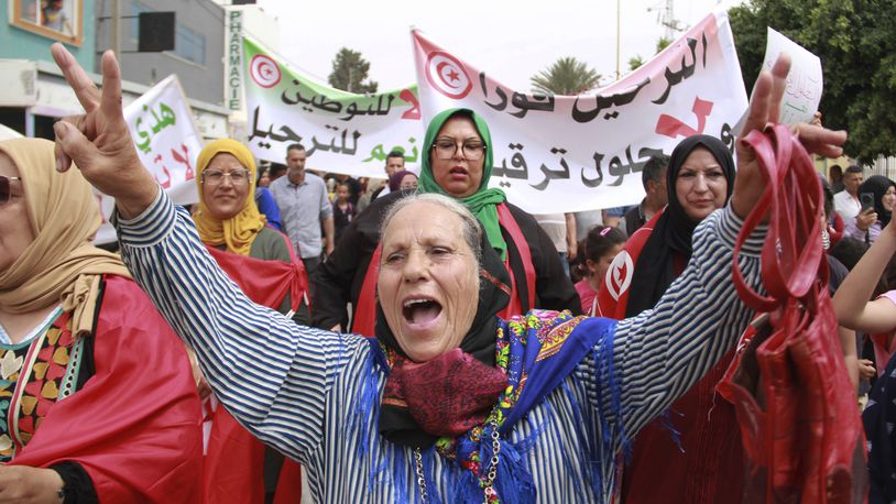 Tunisians take part in a protest against the presence of sub-Saharan migrants who have found themselves stranded as the country ramps up its border patrol efforts, in Jebeniana, Tunisia, Saturday, May 18, 2024. Anti-migrant anger is mounting in olive-growing towns along the Tunisian coastline that have emerged as a launchpad for thousands of people hoping to reach Europe by boat. Banner in Arabic reads "Deportation now." (AP Photo/Houssem Zouari)