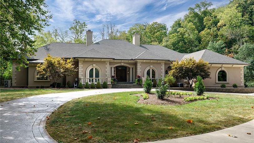 A circular brick paver and concrete driveway winds through the wooded property to the front of the home.