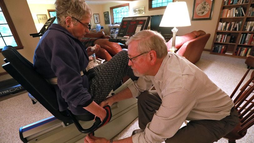 Steve Sidlo helps his wife, Cynthia, get into position on her exercise bike Wednesday in their Springfield home. Cynthia is recovering from a stroke several years ago. BILL LACKEY/STAFF