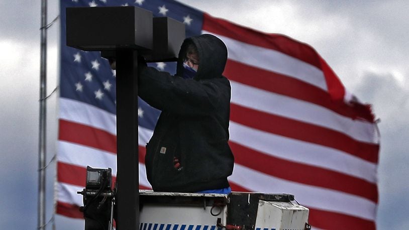 The giant American flag at the Springfield Post Office provided a patriotic backdrop for a worker fixing a light in the parking lot of Shawnee Place Apartments in downtown Springfield. BILL LACKEY/STAFF