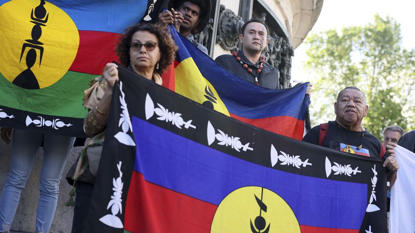 FILE - Demonstrators hold Kanak and Socialist National Liberation Front (FLNKS) flags during a gathering in Paris, Thursday May.16, 2024. A pro-independence movement in the French Pacific territory of New Caledonia is demanding the “release and immediate return” of the Indigenous Kanak leader who was flown more than 10,000 miles to mainland France for pretrial detention. Christian Tein, a leader of the movement known as The Field Action Coordination Unit, and six other Kanak activists are now awaiting trial over their alleged role in recent deadly unrest. (AP Photo/Thomas Padilla, File)