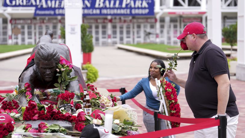 Will Resor, of Anderson Township, Ohio, smells a rose before laying it at the statue of Cincinnati Reds legend Pete Rose, Tuesday, Oct. 1, 2024, in front of Great American Ball Park in Cincinnati. (AP Photo/Kareem Elgazzar)