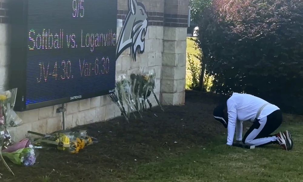 A person kneels in front of flowers that are placed outside the entrance to Apalachee High School on Thursday, Sept. 5, 2024 in Winder, Ga., a day after deadly shootings at the school. (AP Photo/Charlotte Kramon)