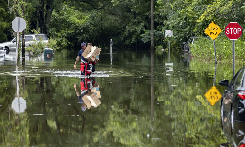 Savannah Fire Advanced Firefighters Andrew Stevenson, front, and Ron Strauss carry food to residents in the Tremont Park neighborhood that where stranded in flooding from Tropical Storm Debby, Tuesday, Aug. 6, 2024, in Savannah, Ga. (AP Photo/Stephen B. Morton)