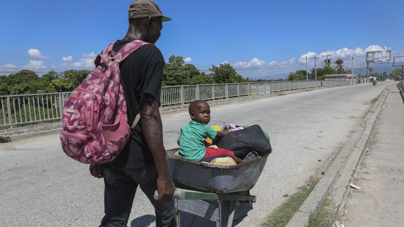 A man pushes a child in a wheelbarrow along a street in Pont-Sonde, Haiti, Monday, Oct. 7, 2024, days after a gang attacked the town. (AP Photo/Odelyn Joseph)