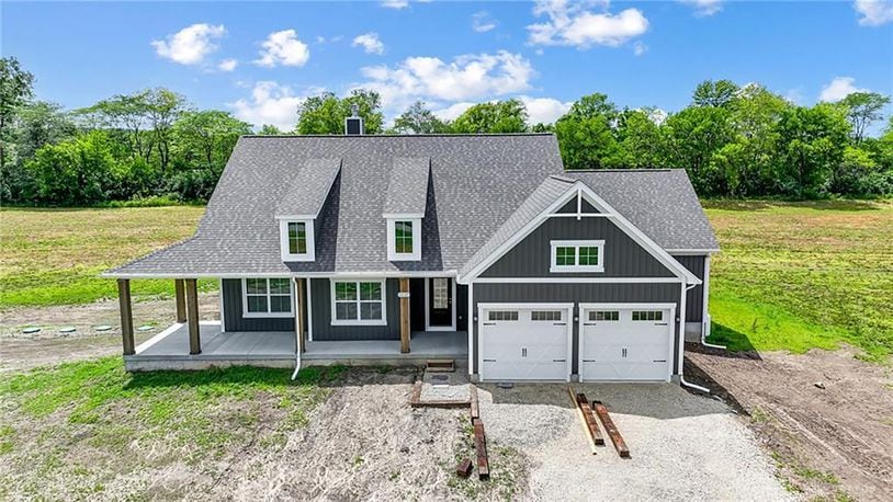 The front of the new construction ranch home has a covered wrap around porch and decorative dormers. It also has a two car attached garage.