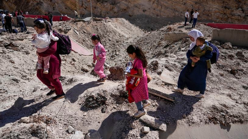 People carry their luggage as they cross into Syria on foot, through a crater caused by Israeli airstrikes aiming to block Beirut-Damascus highway at the Masnaa crossing, in the eastern Bekaa Valley, Lebanon, Saturday, Oct. 5, 2024. (AP Photo/Hassan Ammar)