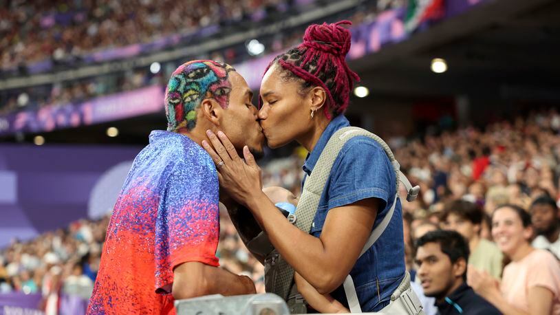 Roderick Townsend of the United States kisses his wife Tynita Townsend, with their son Rodney Townsend, between Rodrick's jumps in the T47 Men's High Jump at the 2024 Paralympics, Sunday, Sept. 1, 2024 in Paris, France. (AP Photo/Caleb Craig)