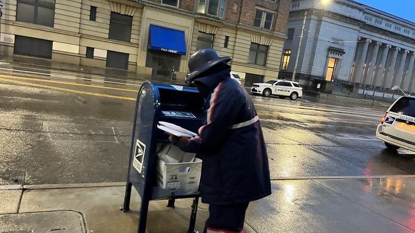 A U.S. postal worker picks up mail from a box in front of City Hall in downtown Dayton. The U.S. Postal Service is hiring city carrier assistants to work at the Dayton Main Post Office. CORNELIUS FROLIK / STAFF