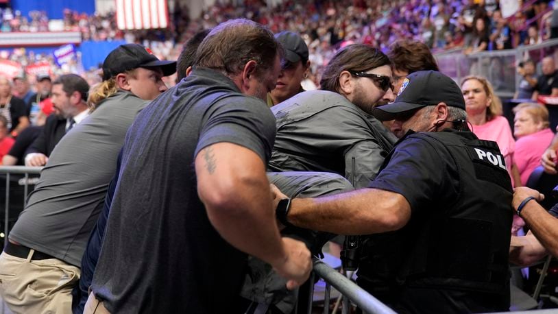 Police remove a man, center with sunglasses, who had climbed onto the media riser, as Republican presidential nominee former President Donald Trump speaks at a campaign event, Friday, Aug. 30, 2024, in Johnstown, Pa. (AP Photo/Alex Brandon)