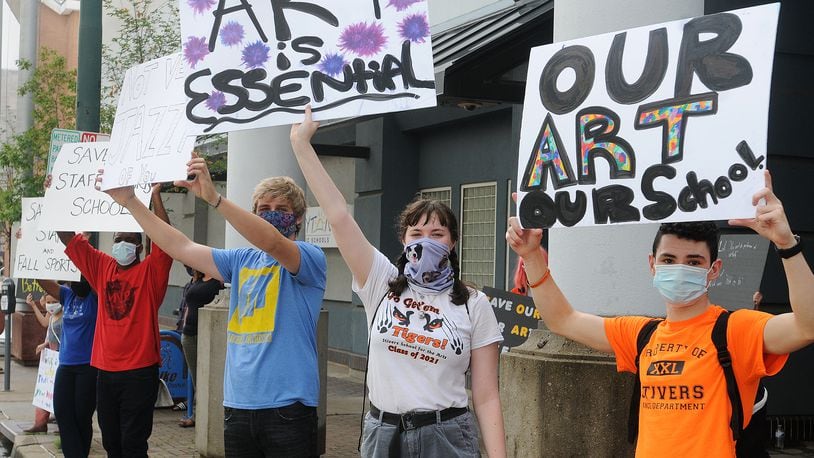 A crowd of people protest layoffs of teachers, especially in the arts, outside the Dayton Public Schools headquarters building on Ludlow Street Aug. 28, 2020.