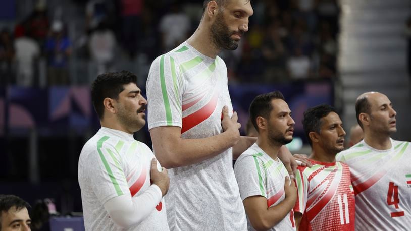 Irans's Morteza Mehrzadselakjani, fourth from right, stands with his teammates on the men's sitting volleyball team as the Iranian national anthem plays before their preliminary game against Brazil during the Paralympic Games in Paris, Sunday, Sept. 1, 2024. Iran won the game in straight sets. (AP Photo/Avni Trivedi)