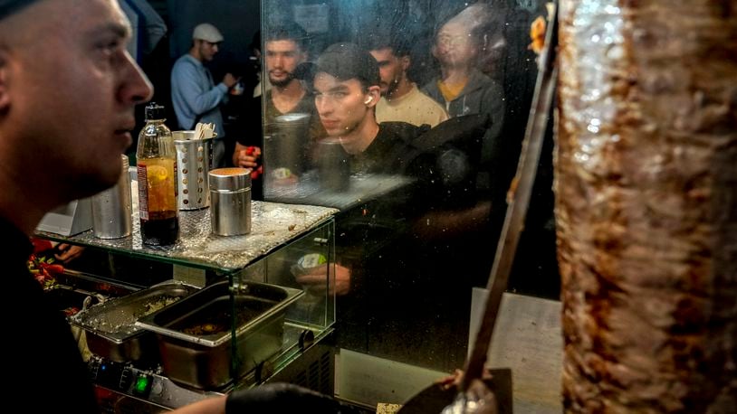 People stand in the line to buy doner kebab while the Turkish cook prepares the doner kebabs, in Berlin, Germany, Wednesday, Sept. 18, 2024. (AP Photo/Ebrahim Noroozi)