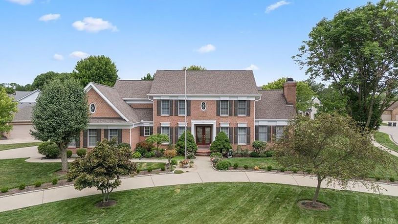 The front of the brick colonial style two story has a circular driveway, three car attached side entry garage and heavy landscaping.