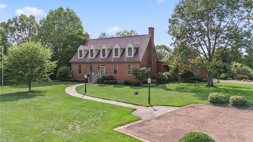 The front of the Cape Cod style brick story and a half has dormers, brick paver walkway and brick steps leading to the front door.