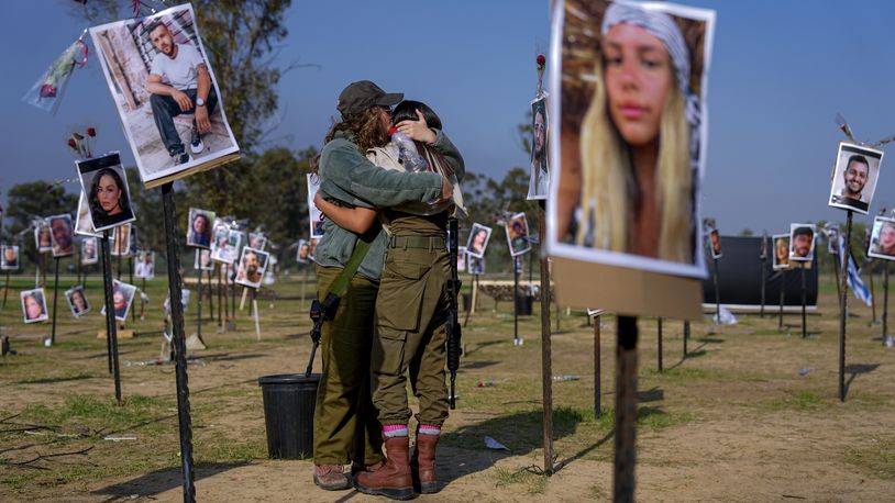 Israeli soldiers embrace next to photos of people killed and taken captive by Hamas militants during their violent rampage through the Nova music festival in southern Israel, which are displayed at the site of the event, to commemorate the October 7, massacre, near kibbutz Re'im, Friday, Dec. 1, 2023. (AP Photo/Ariel Schalit)