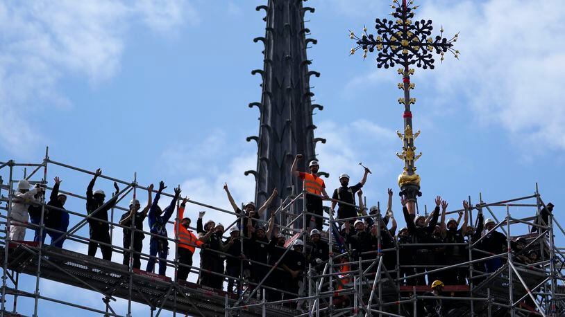 Workers celebrate after reinstalling the Notre Dame de Paris cathedral's Croix du Chevet, right, Friday, May 24, 2024, in Paris. The Croix du Chevet is the only piece of the cathedral roof that did not burn in the devastating April 2019 fire. (AP Photo/Thibault Camus)